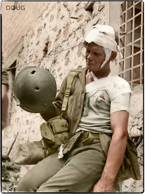 Американский солдат, пострадавший во время боёв в Италии, рассматривает каску, спасшую ему жизнь